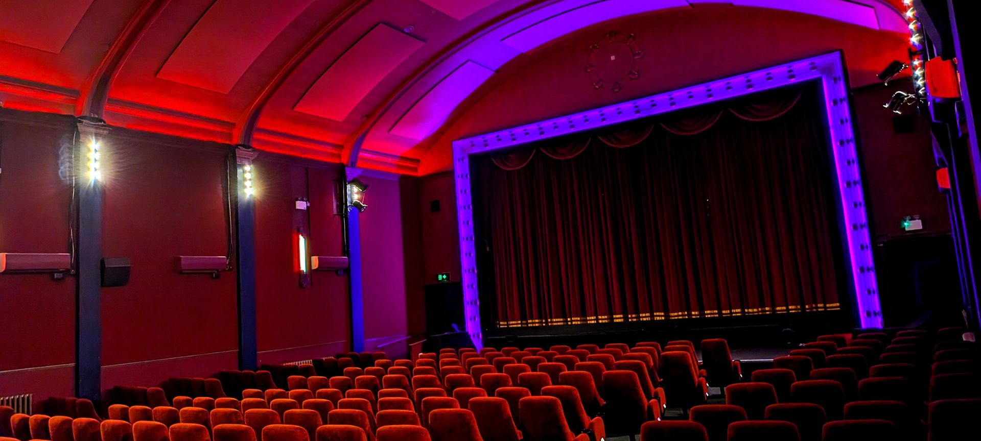 Inside the Duke of York's Picturehouse auditorium, red seats facing a lit stage and velvet curtain