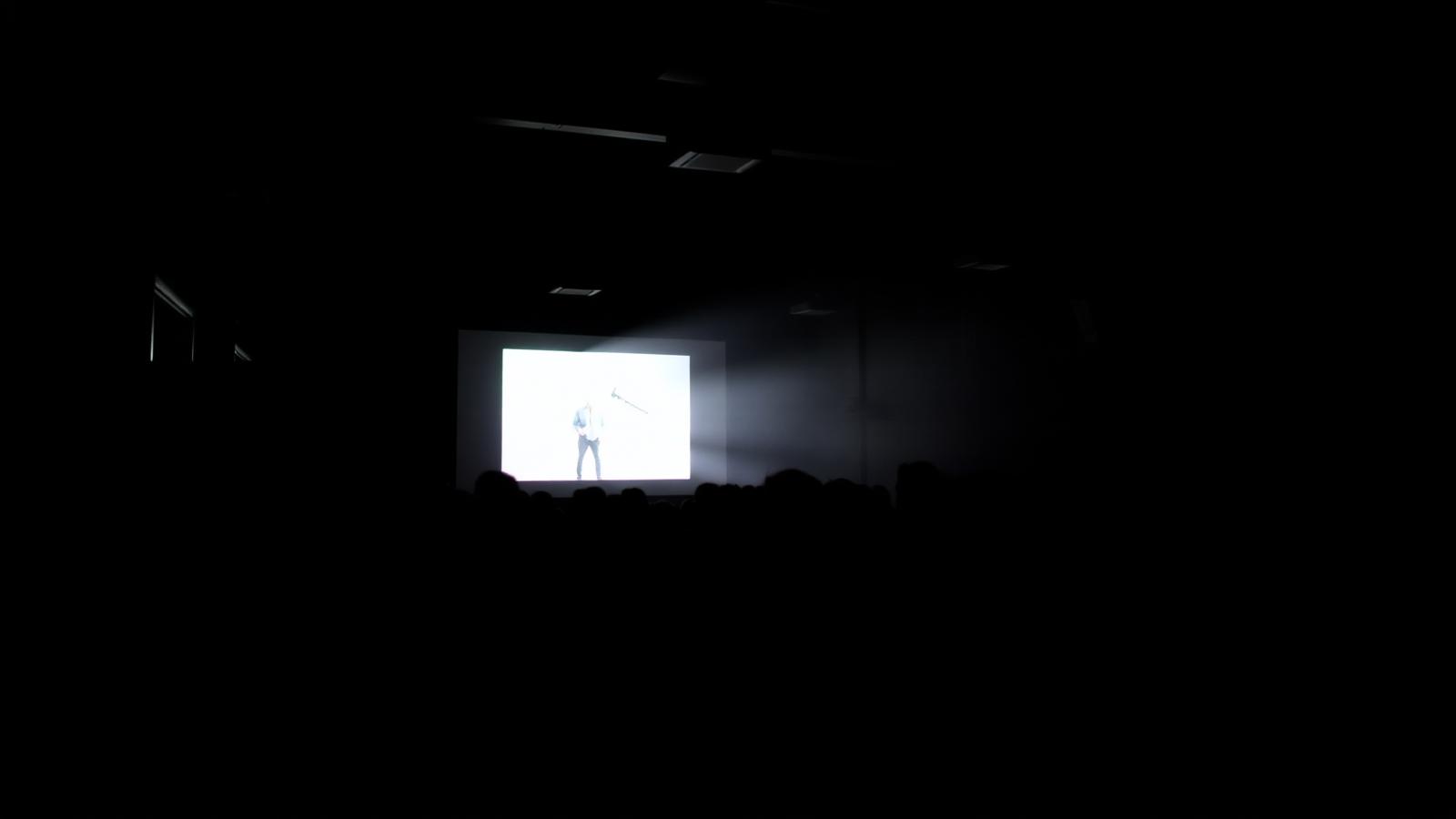 An audience watching a film projected in a darkened hall